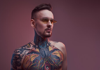 Shirtless and bearded bearded and tattooed guy with stylish hairstyle and sunglasses poses in...