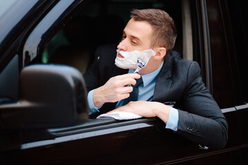 Businessman shaving in car by razor and foam at the wheel. Shaving man in the driver's seat....