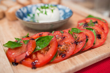 Delicious sliced tomatoes served on a wooden board with fresh basil leaves and balsamic vinegar. Professional serving.