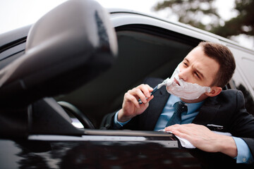 Businessman shaving in car by razor and foam at the wheel. Shaving man in the driver's seat....