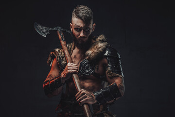Fototapeta na wymiar Dressed in light armour with fur scandinavian seafarer armed with two handed axe poses in dark background.