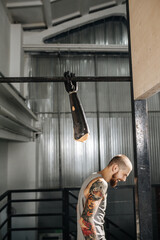 Joking cyborg man left disconnected bionic hand hanging on a workout bar as a prank. Beautiful tattoos on shoulders. Side view.