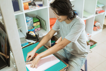 Young male entrepreneur working in a stationery shop. cutting up paper
