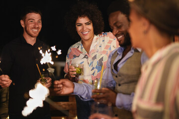 Happy multiracial people celebrate new year's eve together outdoor with sparklers and cocktails