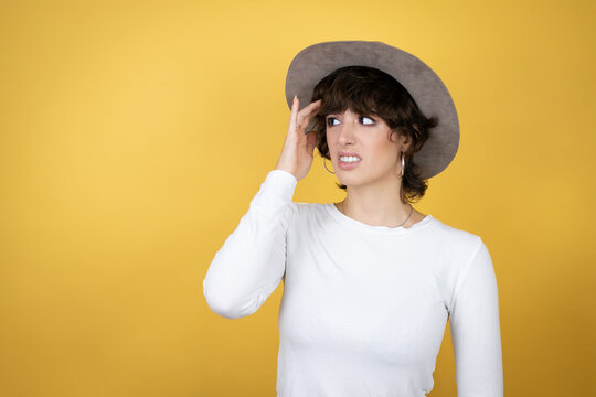 Young caucasian woman wearing hat over isolated yellow background confuse and wonder about question. Uncertain with doubt, thinking with hand on head