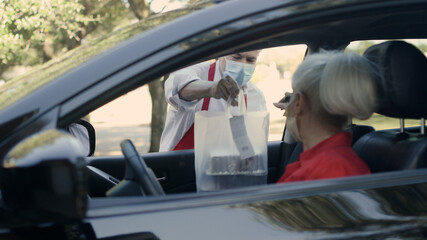 Masked up due to COVID woman receives her curbside food order - obrazy, fototapety, plakaty