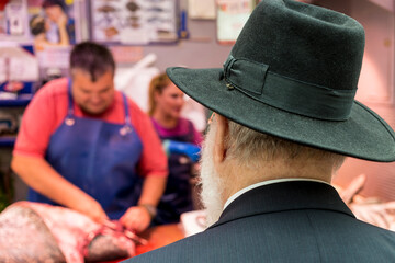 Back cropped over the shoulder view of bearded man in black hat and jacket standing in front of a...