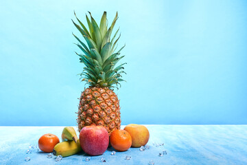 Pineapple surrounded by fruit on blue background with copy space