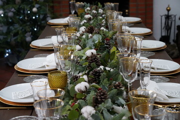 Christmas or New Years celebration party table setting. Plates, golden cutlery, glasses, gift box, festive branch decoration