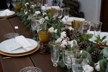 Christmas or New Years celebration party table setting. Plates, golden cutlery, glasses, gift box, festive branch decoration