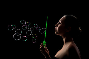 Young girl is blowing soap-bubbles on the black background
