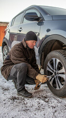 A man replaces car wheels with summer tires for winter ones near the garage.
