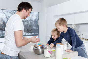 A young dad with small children in a large bright kitchen are preparing dough cookies. Love and tenderness in the family.