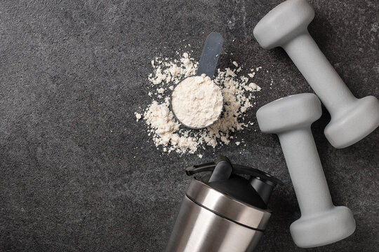 Whey protein powder, shaker and dumbbells on black