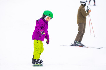 Fototapeta na wymiar Little Cute Girl Snowboarding at ski resort in sunny winter day.