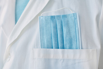 Medical professional with protective face mask in white coat pocket