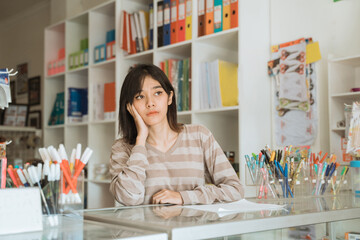 Portrait boring young girl entrepreneur waiting customer working in a stationery shop.