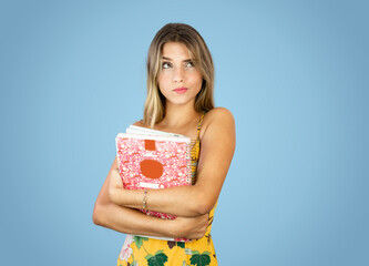 Caucasian student girl with school books in hands. Blue Background. Expression of indecisiveness.