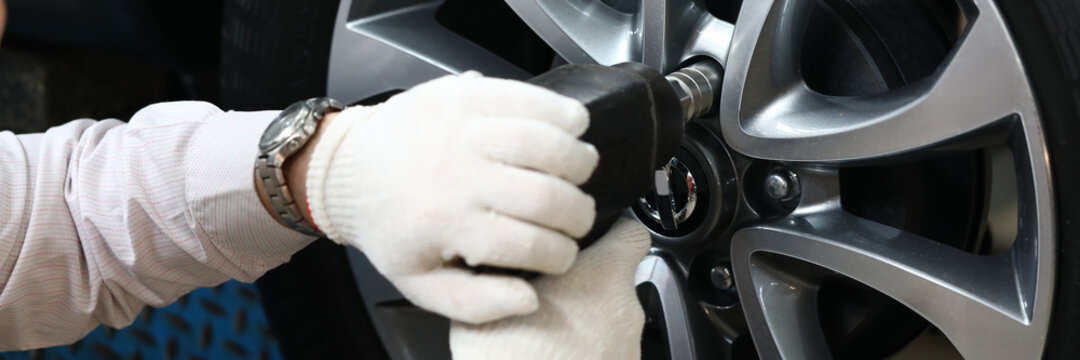 Close up of male hands in white gloves using impact wrench while installing car wheel lug nuts