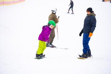 Fototapeta na wymiar Snowboard Winter Sport. little girl learning to snowboard, wearing warm winter clothes. Winter background.