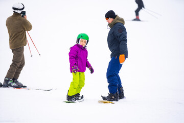 Instructors teach a child on a snow slope to snowboard