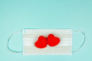 Two red hearts on medical protection mask on light blue background, top view. Concept of healthcare, self-defense. Creative flat lay with copy space