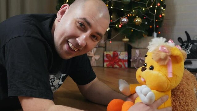 A man holds a teddy bear, near a Christmas tree. freaky people concept. play with a toy. soothing toy for autism