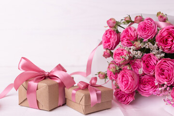 Fototapeta na wymiar Fresh pastel soft pink roses, and gift boxes wrapped in kraft papper with ribbons on white wooden table.
