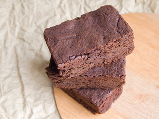 Delicious homemade chocolate cake. Three pieces of brownie stacked in a pile on a calm beige background. Simple and tasty dessert.