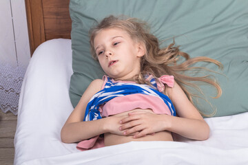 studio lighting. a girl of school age lies in bed and holds on to her stomach. Close-up.