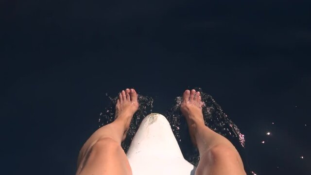 Womans feet in sea during moves boat. Young woman sitting on a bow of yacht. FPV anf slow motion footage.
