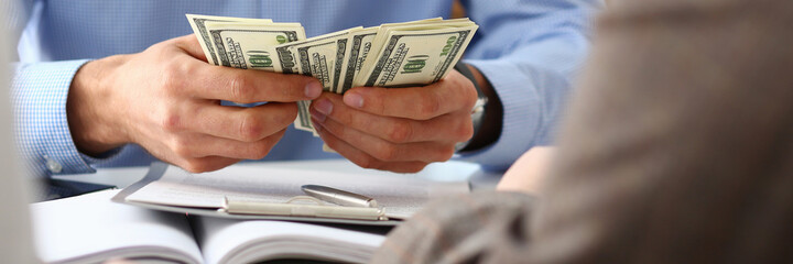 Close up of bank male worker in shirt holding dollars while sitting at the table with documents in...