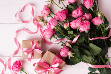 Fresh pastel soft pink roses, and gift boxes wrapped in kraft papper with ribbons on white wooden table.