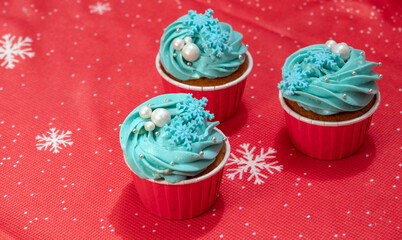 Three cupcakes decorated with cream, beads and snowflakes. New year's dessert. Red background. Selective focus.