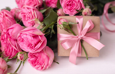 Fresh pastel soft pink roses, and gift boxes wrapped in kraft papper with ribbons on white wooden table.