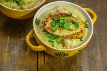 dietary mashed cauliflower in ceramic bowls seasoned with parsley and croutons on a wooden table