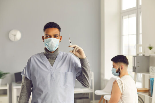 Young black man doctor nurse in medical face fask holding syringe with vaccination against COVID-19
