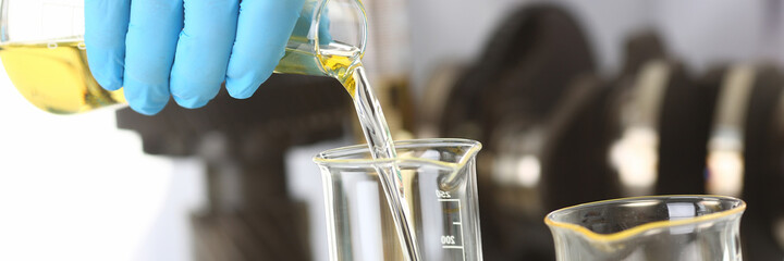 Close up of male hands in blue sterile gloves pouring yellow liquid into glass tube in laboratory