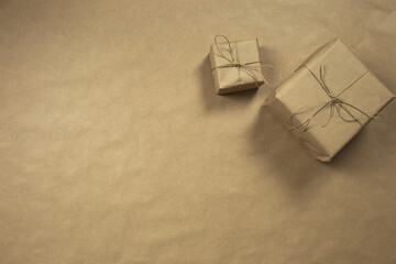 Two gift boxes wrapped in plain brown recycled paper with rope on brown background texture top view, present and recycle concept, copy space, space for text