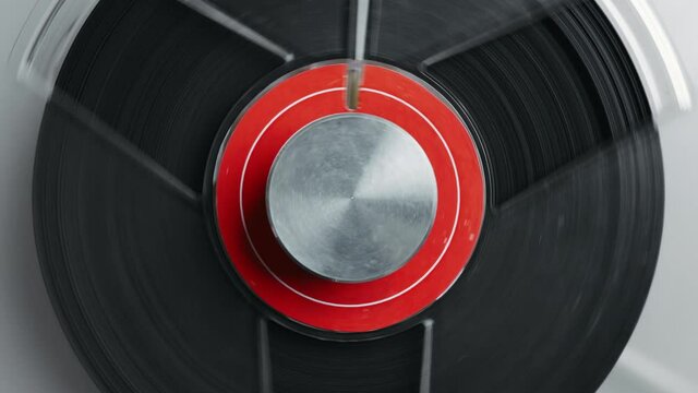 Reel to reel tape recorder playing. Rotating vintage music player close up. Retro tape. Spinning reels metallic color with red disc. View from above. Popular Disco Trends 60s, 70s, 80s, 90s.