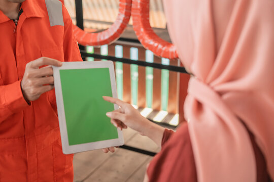 Close up of a mechanic in wearpack wearing a digital tablet with a customer in the background of a tire rack