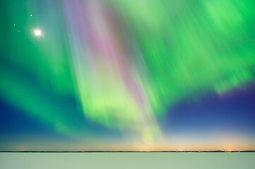 Aurora Borealis and Moon above frozen lake after sunset