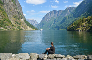 Fototapeta na wymiar Man sitting and enjoying view on the lake and fjords in clear summer day. Gudvangen, Sognefjord, Norway