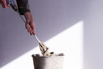 stirrer in the hand of a worker in a cement mortar and an old rusty bucket close up