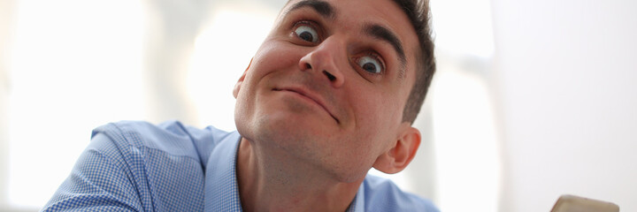 Close up of gentleman in blue shirt looking at camera with wide opened eyes and smiling while holding smartphone