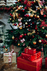 Stacks of Christmas presents in red paper under a Christmas tree decorated red and golden balls near fireplace in living room .New Year interior