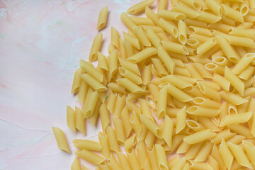 Pile of raw traditional Italian penne pasta. Pink background. Close up, copy space