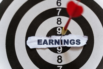 A piece of paper with the text is nailed to the target with a dart - EARNINGS