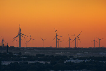 Wind turbine power generators silhouettes at ocean coastline at sunset. Alternative renewable energy production.