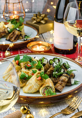 Holiday snacks with zucchini and eggplant rolls on wooden table served with plates, glasses, bottle of wine, candles, festive decoration. Christmas and New Year food, bokeh, light
